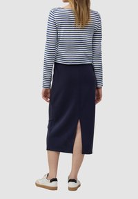 Marineblauwe midi-rok met een zijsplit, gecombineerd met een gestreepte blouse met lange mouwen in blauw en wit. Model draagt witte sneakers met zwarte accenten.