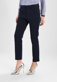 Marinblå skräddarsydda byxor med slim fit och slät textur, med bältesloopar och sidofickor, i kombination med silverfärgade högklackade skor.