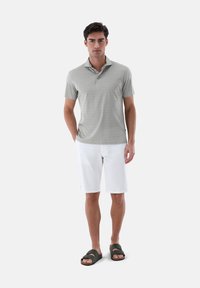 Helles graues Polohemd mit Muster, weiße Shorts und dunkelgrüne Rutschsandalen. Das Polo hat einen Kragen und eine zwei-Knopf-Leiste. Glatte Textur.