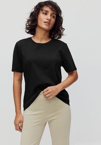 Musta lyhythihainen t-paita, joka on valmistettu sileästä kankaasta ja jossa on pyöreä kaula-aukko, yhdistettynä vaaleanbeigeihin slim-fit-housuihin, joissa on rento leikkaus.