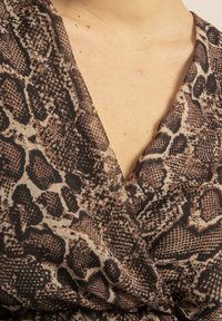 Top enveloppé dans un imprimé serpent comprenant des nuances de marron, noir et beige. Tissu doux et texturé avec des touches subtiles de fil doré.