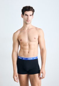 Boxers negros con una cinturilla azul de Nike. El material parece suave, con un diseño ajustado, que presenta un logo en el frontal y en la cinturilla.
