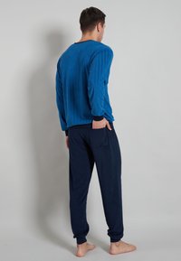 Blue ribbed long-sleeve top with a round neckline, paired with dark navy pants featuring a back pocket. Soft texture, relaxed fit.