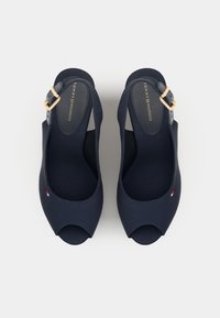 Zapatos peep-toe azul marino con parte superior de tela suave, correa en el tobillo ajustable y hebilla dorada. Presenta un pequeño logo en el lado.