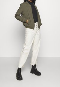Olive green bomber jacket, black top, cream wide-leg trousers, and black platform boots. Simple design, smooth texture, and button details.