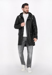 Juodas vandeniui atsparus džemperis su kapišonu, priekyje su užtrauktuku, mygtukais ir kišenėmis; derinamas su pilkais džinsais ir baltais sportbačiais.