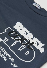 Navyblaue T-Shirt mit auffälligen weißen und schwarzen Textgrafiken, rundem Ausschnitt und geripptem Muster. Betonung auf Grafikdesign und Farbkombination.