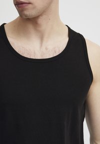 Schwarzes ärmelloses Tank-Top aus Baumwolle, mit rundem Ausschnitt und glatter Textur, eng anliegend am Körper ohne sichtbare Muster.