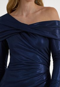 Μπλε σκούρο φόρεμα με ακάλυπτους ώμους και μαζεμένη υφή, κατασκευασμένο από γυαλιστερό ύφασμα, με στριφτό σχέδιο στο λαιμό και εφαρμοστή σιλουέτα.