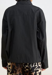 Svart jacka med avslappnad passform, med krage och ryggsämsdetalj, kombinerad med en leopardmönstrad kjol. Slät textur, minimal design.