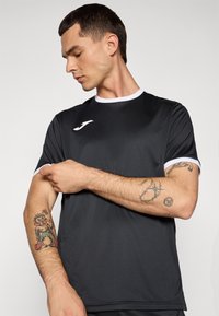 Schwarzes Sport-T-Shirt mit weißen Akzenten, Rundhalsausschnitt, kurzen Ärmeln und glatter Textur. Verfügt über ein Logo auf der Brust und ein Tattoo am Arm.