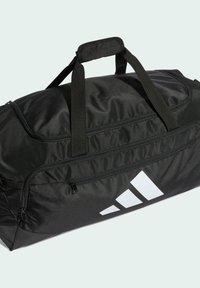 Čierna cestovná taška z odolnej tkaniny, so dvoma hornými rúčkami, hlavnou komorou na zips a bielym logom Adidas na jednej strane.