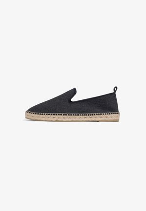 Alpargata negra tipo slip-on con suela de yute tejido y lazo de tela en el talón, mostrada sobre fondo blanco en perfil lateral.