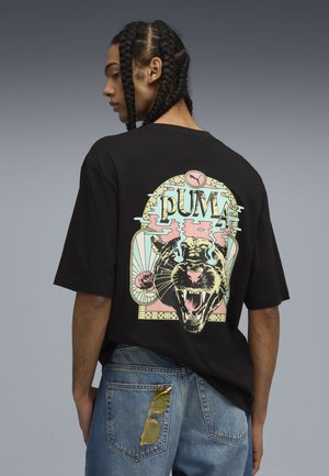 Sort bomuld t-shirt med et stort, farverigt grafisk tryk af en brølende panter med rosenakcenter, båret sammen med bløde denim jeans og solbriller.