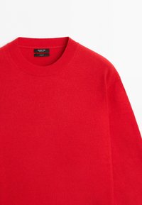 Pull en cachemire rouge vif à col rond et manches longues, vu de l'avant supérieur, avec col côtelé visible et étiquette de marque à l'intérieur.