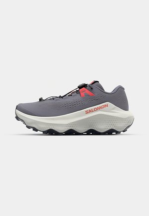 Leichter grauer Trailrunning-Schuh mit einer strukturierten Oberseite, roten Akzenten und einer dicken weißen Zwischensohle, die eine robuste schwarze Außensohle aufweist.