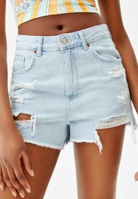 Vaaleansiniset farkkushortsit, joissa on kulutettuja repeämiä, rispaantuneet reunat ja klassinen viiden taskun malli. Vyötäröllä hopeanvärinen nappikiinnitys.