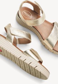 Goldfarbene Metallic-Sandalen mit offenen Zehen, verstellbaren Klettverschlüssen, gepolsterten braunen Innensohlen und beigen, strukturierten Gummisohlen.