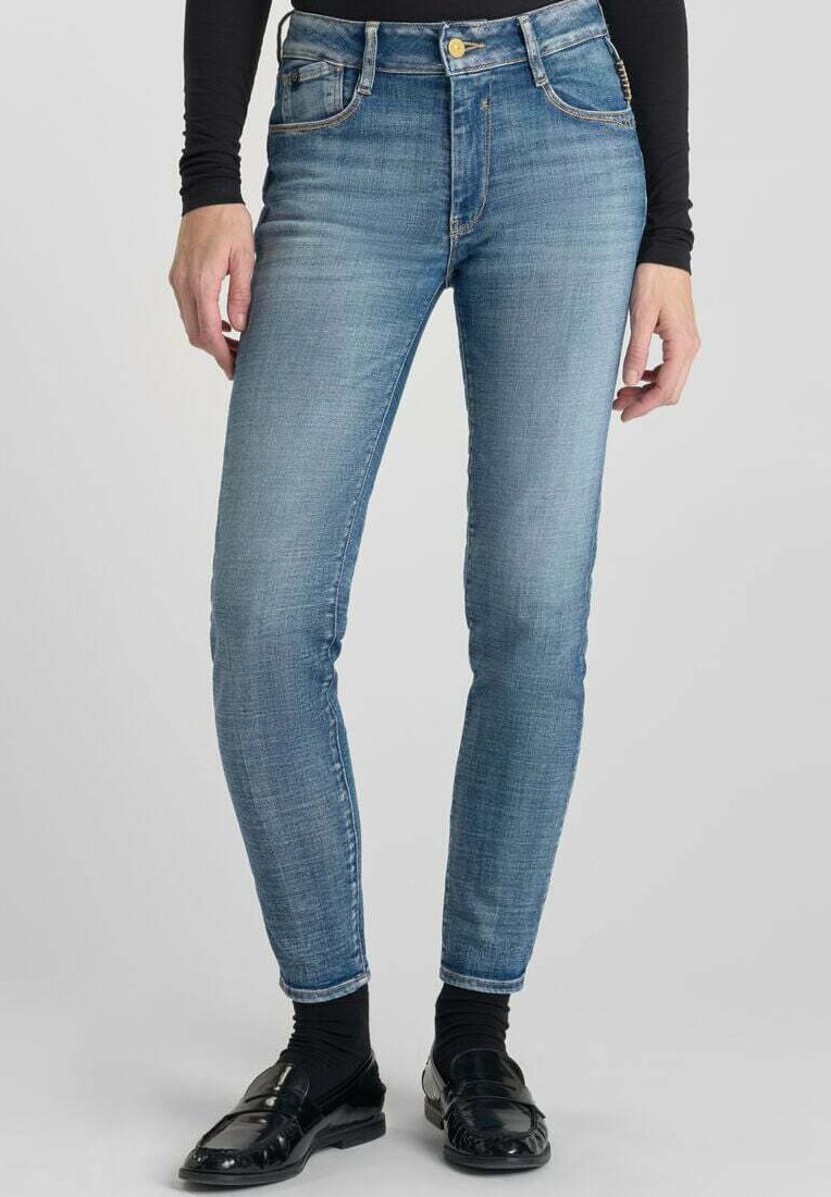 Jeans slim fit en denim bleu. Caractéristiques : taille haute, décoloration subtile, cinq poches et fermeture à bouton en laiton. Stylé avec des chaussures noires.