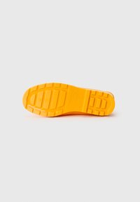 Semelle de chaussure en caoutchouc jaune vif avec des motifs de grip texturés et un profil défini. Présente des imprints de marque sur le côté.