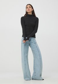 Maglione a collo alto a coste di carbone, vestibilità slim, abbinato a jeans a gamba larga blu chiaro a vita alta, con dettagli di cucitura visibili.