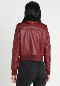 Burgunderfärgad läderjacka i croppad modell med en svart fårskinnskrage; har ribbade mudd och midja, slät yta och synlig sömnad.