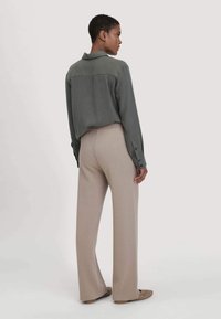 Olivgrüne Button-up-Hemd mit Rückenpasse, kombiniert mit beigen weit geschnittenen Hosen. Eine glatte Textur, lockere Passform und schlichtes Design.