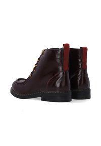 Burgunderfarbene Leder-Stiefeletten mit runder Spitze, goldenen Ösen, roten Textil-Hinterkappen und contrasting schwarzer Gummisohle.