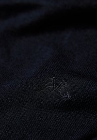 Tessuto lavorato a maglia di colore blu navy con una texture liscia, caratterizzato da un logo ricamato discreto. Il design è semplice e uniforme in tutta la superficie.