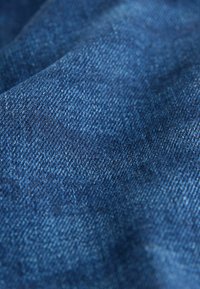 Blåt denimstof med en glat tekstur og et subtilt mønster af twillvævning. Farverne varierer fra mørk til lyseblå.