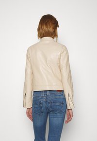 Beige läderjacka med en åtsittande design, quiltat detaljerat bakstycke och dragkedjevärmar, kombinerat med blå denimjeans.