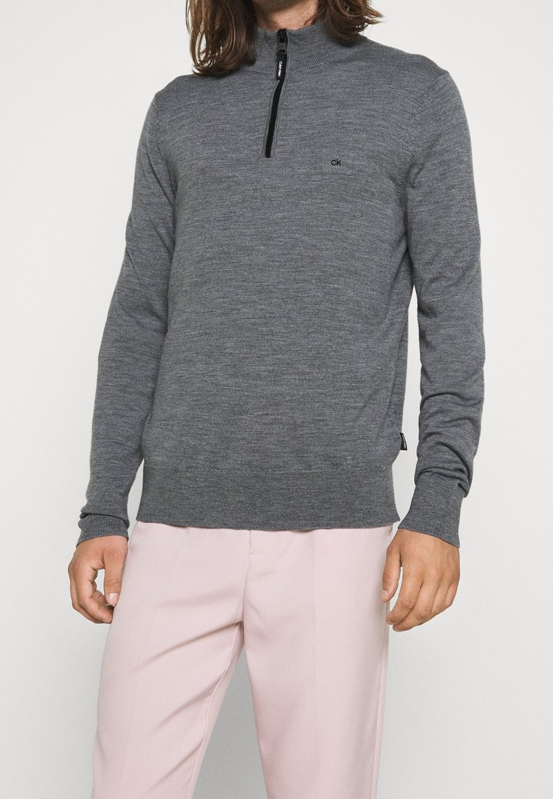 Grau langärmliger Pullover mit einem halben Reißverschlusskragen, gerippten Bündchen und Saum. Mit einem dezenten Logo auf der Brust und glatter Stofftextur.