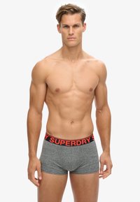 Caleçons boxers gris avec une taille noire arborant le texte rouge "SUPERDRY". Tissu doux et extensible avec une coupe ajustée.