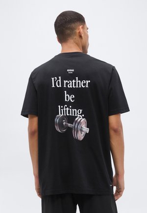 Άνδρας που φοράει μαύρο T-shirt Adidas με το κείμενο «Θα προτιμούσα να σηκώνω βάρη» και γραφικό μιας αλτήρας στην πλάτη, γυρισμένος με την πλάτη στην κάμερα.