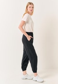 Zwarte joggingbroeken met elastische tailleband en boorden, gecombineerd met een wit t-shirt en witte sneakers. Gladde stof, casual pasvorm.