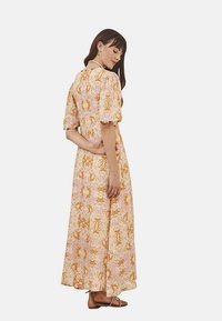 Vestido maxi en tejido ligero con un patrón floral en tonos naranjas y rosas, manga corta abullonada y un corte relajado que llega a la mitad de la pantorrilla.