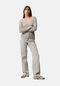 Grauer Strickcardigan mit Reißverschluss, langen Ärmeln und V-Ausschnitt. Kombiniert mit hellgrauen weiten Jeans und sportlichen grauen Sneakers.