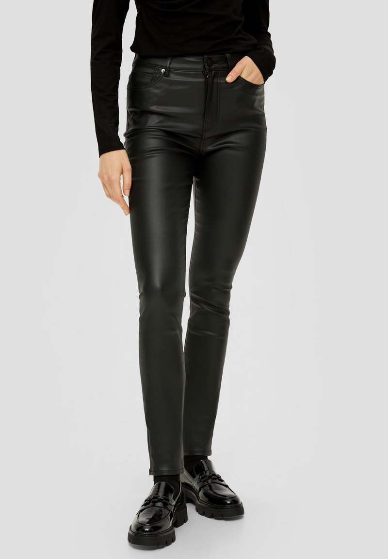 Crne visokotajnice skinny hlače od umjetne kože, uparene s crnom dugom majicom i crnim debelim loafers cipelama na svijetloj pozadini.