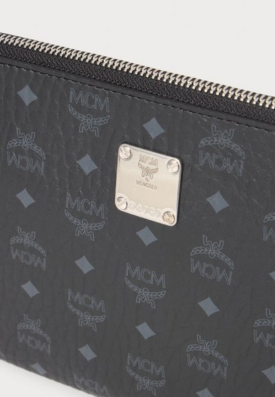 Portefeuille en cuir noir avec une fermeture éclair argentée et une plaque métallique gravée du logo MCM München et du numéro de série R4787.