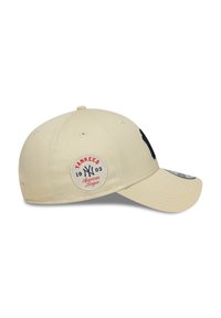 Beige színű baseball sapka, strukturált koronával, hímzett tengerész-kék logóval, valamint egy folttal, amelyen piros és kék színnel szerepel a "Yankees" és az "American League" felirat.