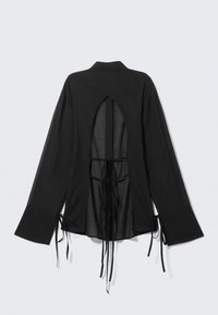 Chemise noire à manches longues avec un dos découpé, des liens ajustables et des poignets évasés. Fabriquée en tissu léger et transparent.