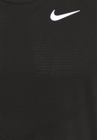 Débardeur de sport noir en tissu texturé, avec un logo Nike blanc sur la poitrine gauche et un motif subtil partout.