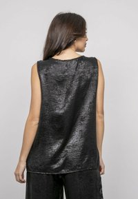 Haut sans manches noir en tissu brillant, présentant un design simple avec un col rond et une coupe légèrement ample.