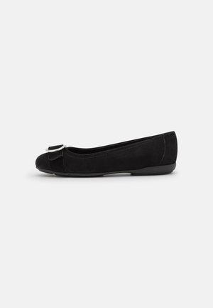 Schwarzer, flacher Ballettschuh mit abgerundeter Spitze, dekorativer Schleife und silberner Schnalle vorne, von der Seite auf weißem Hintergrund gezeigt.