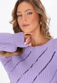 Maglione lavorato a maglia lilla con motivi a diamante testurizzati e decorazioni metalliche verticali sulla parte anteriore. Polsini lisci a coste.