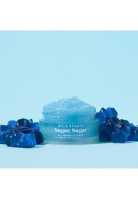 Klar krukke med ljusblå läppskrubb inuti, märkt "Sugar, Sugar." Omgivande blå gummiformer förstärker den livliga färgskalan.