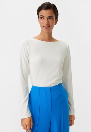 Long-sleeve white top with a wide boat neckline, paired with high-waisted bright blue trousers featuring front pleats and smooth fabric texture.