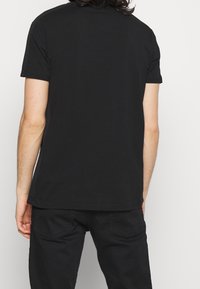 Černé bavlněné tričko s krátkým rukávem, s kulatým výstřihem, hladkou texturou a rovním lemem v pase. Jednobarevné, bez vzorů.
