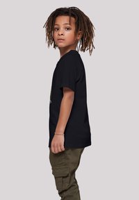 Black t-shirt with short sleeves, featuring a round neckline. Worn with olive green cargo pants. Child with shoulder-length, textured hair.