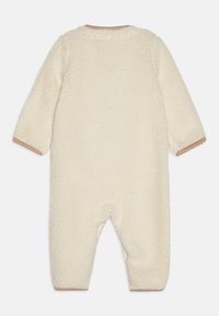 Cremefarbener Fleece-Overall mit langen Ärmeln, strukturierter Oberfläche und braunen Akzenten an den Bündchen. Verfügt über einen runden Ausschnitt und einen Fußdesign.